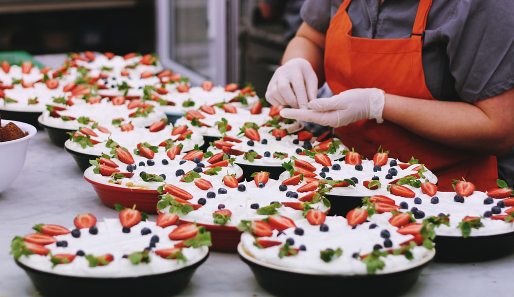 Person decorating food bowl with fruit while wearing gloves